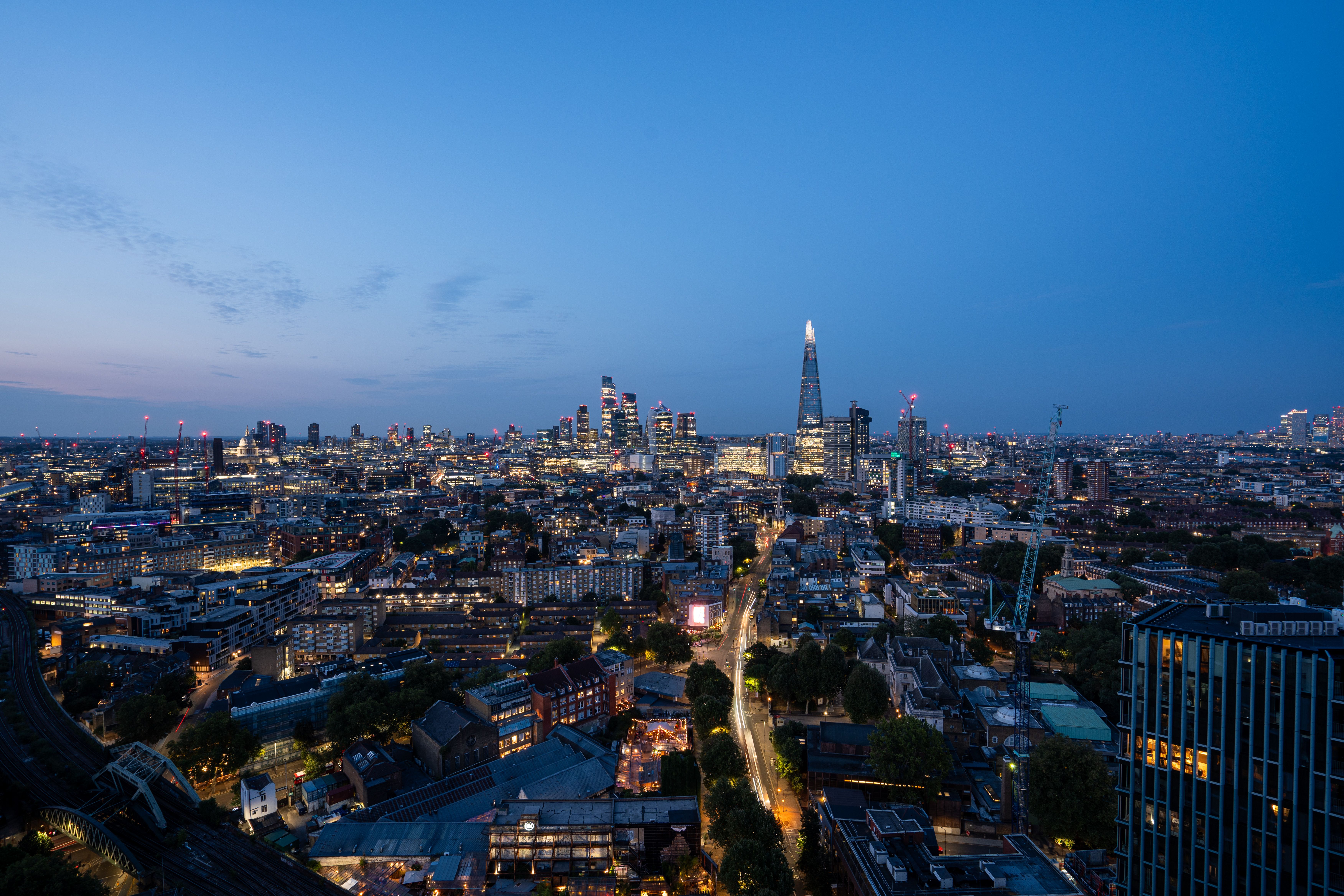 A minimalist high-end private office interior featuring a dark wood desk and panoramic city views at dusk.