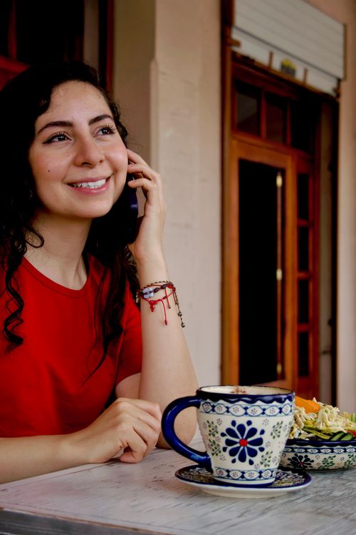 Free Smiling woman in red shirt talking on phone and enjoying coffee at a café. Stock Photo