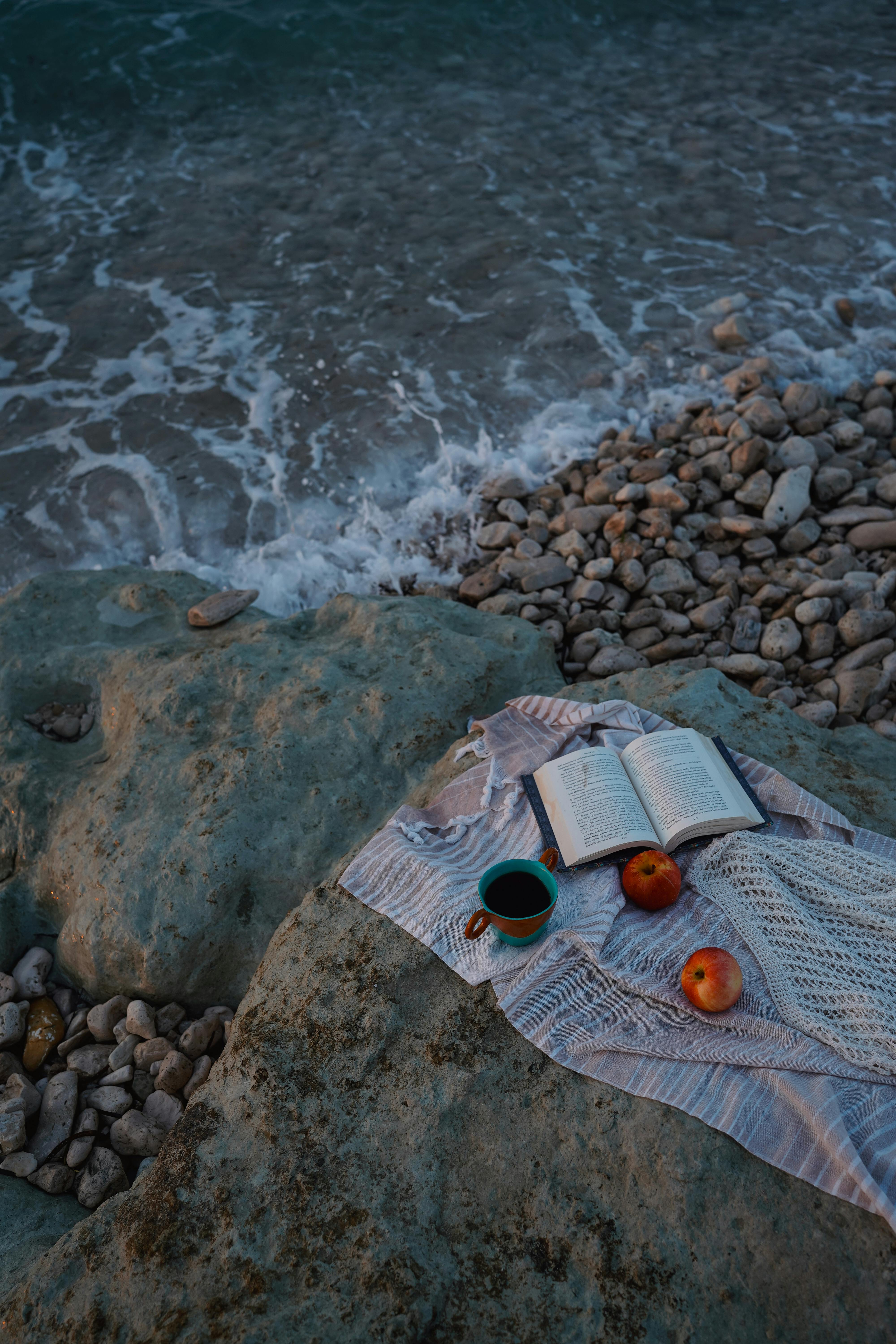 Serene beach setting with a book, apples, and coffee for a relaxing sunset picnic.