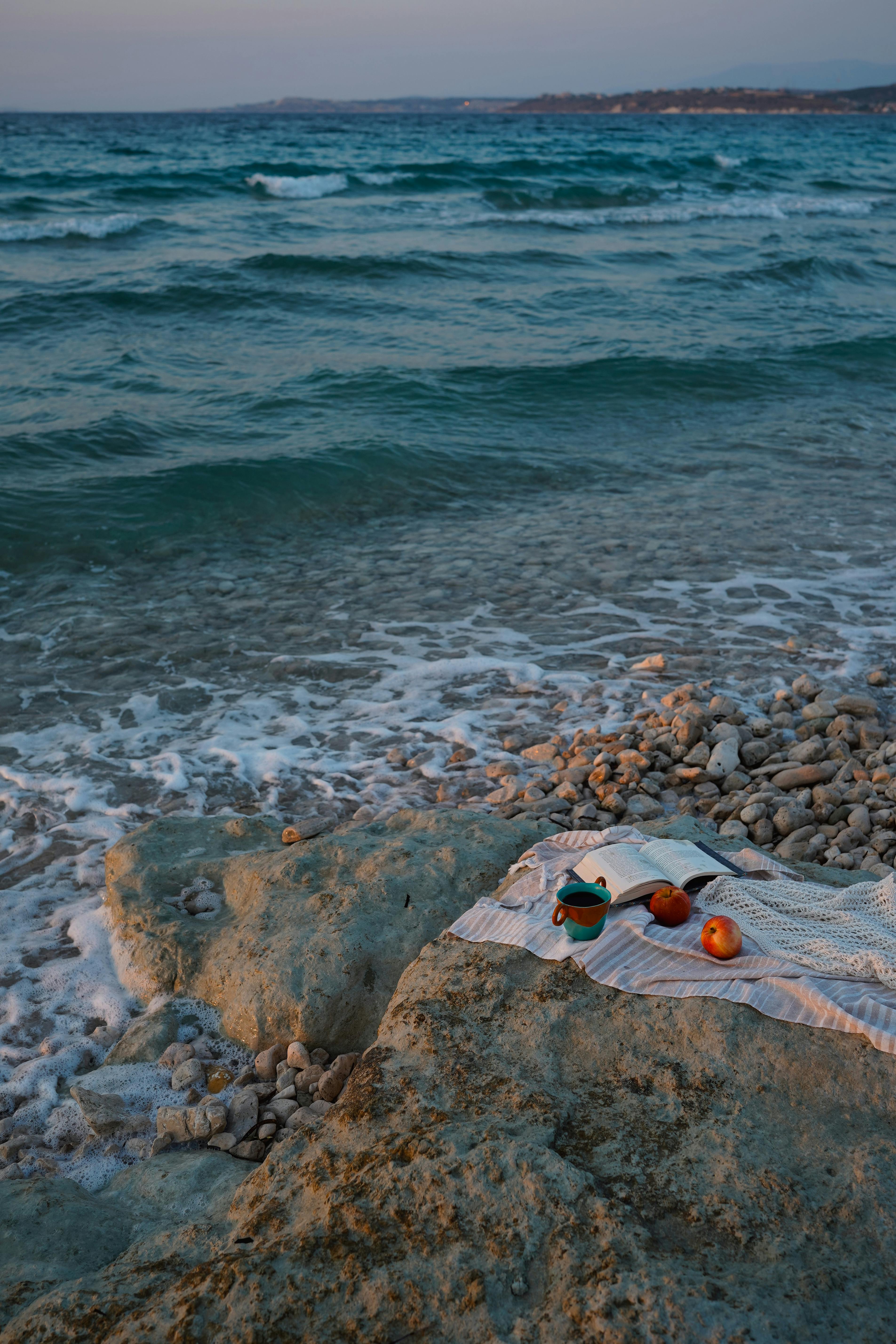 A peaceful twilight beach scene with a picnic on rocks by the ocean waves.