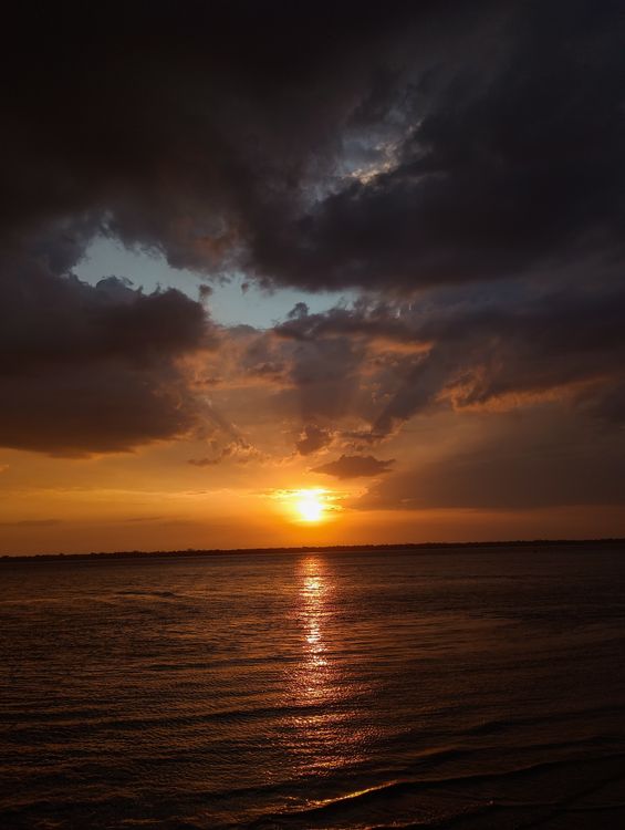 A sunset over the ocean with dark clouds · Free Stock Photo