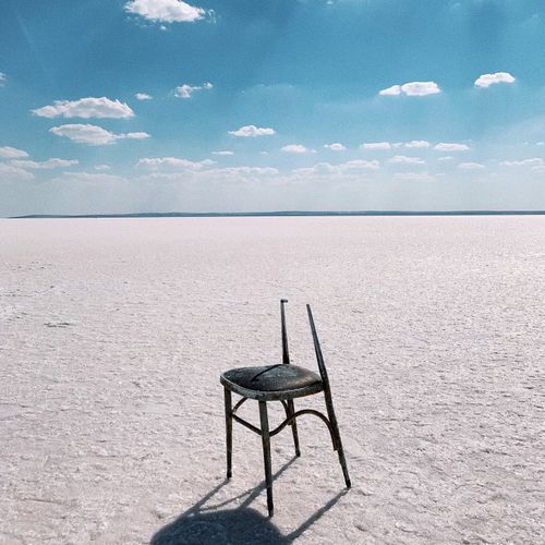 Free A lone chair sits on an expansive salt flat under a beautiful blue sky with scattered clouds. Stock Photo