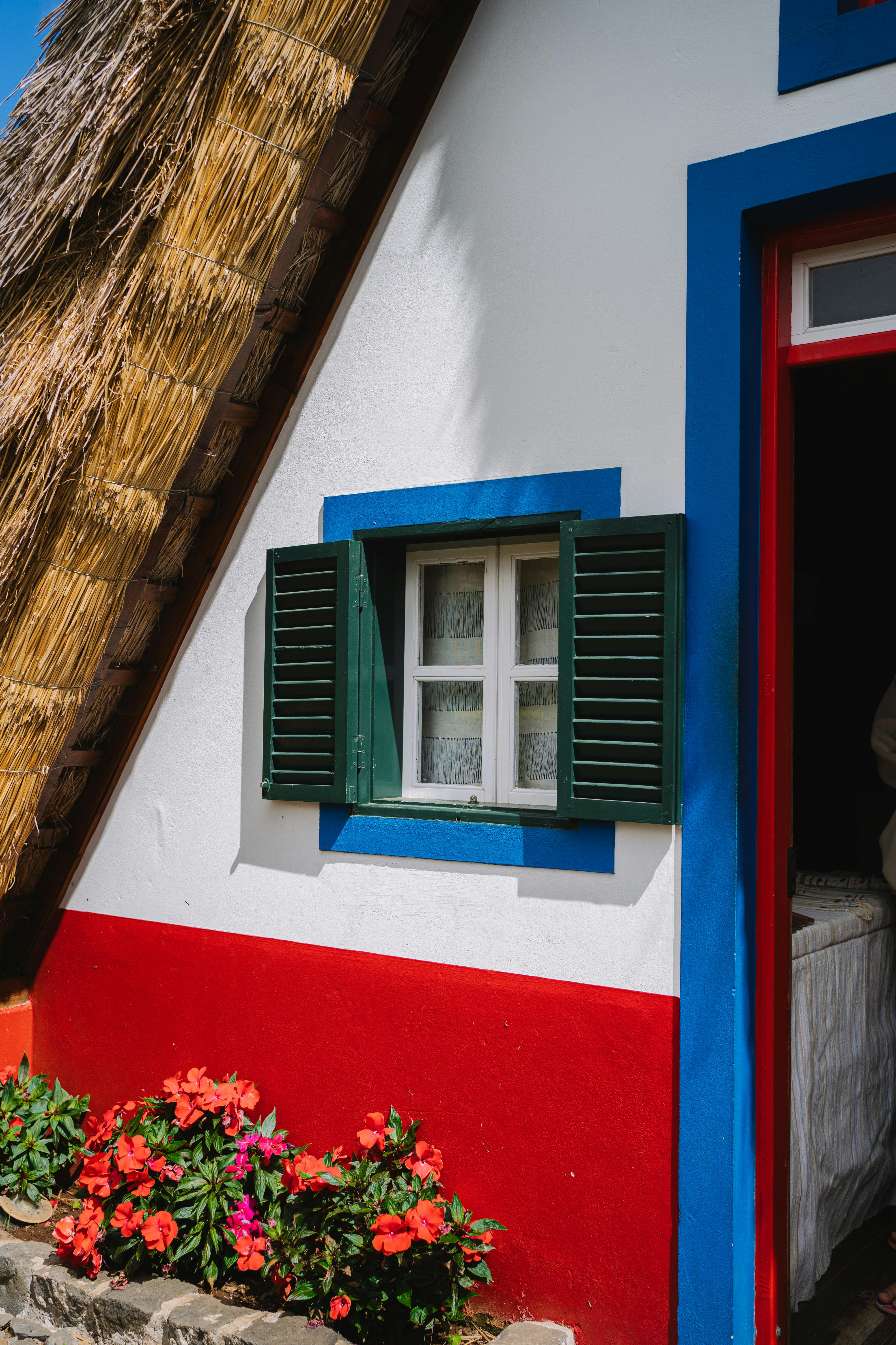 Charming traditional house with thatched roof and vibrant colors, featuring a green shuttered window.
