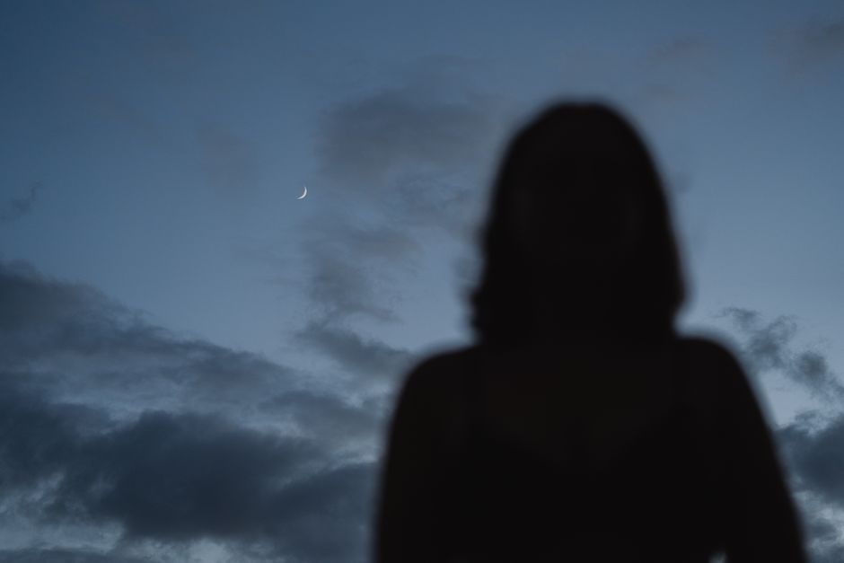A mysterious silhouette of a woman against a twilight sky with a visible crescent moon.
