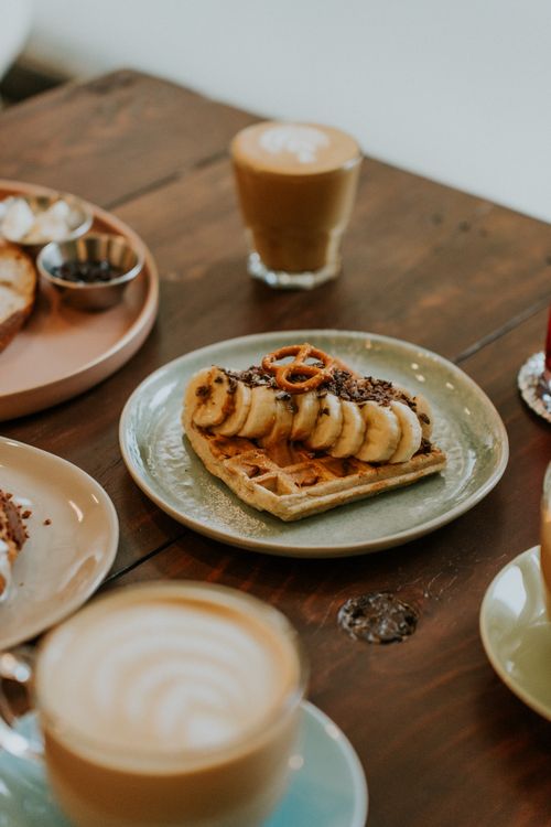 Free A tasty breakfast spread featuring a waffle topped with banana slices and pretzel, accompanied by hot coffee. Stock Photo