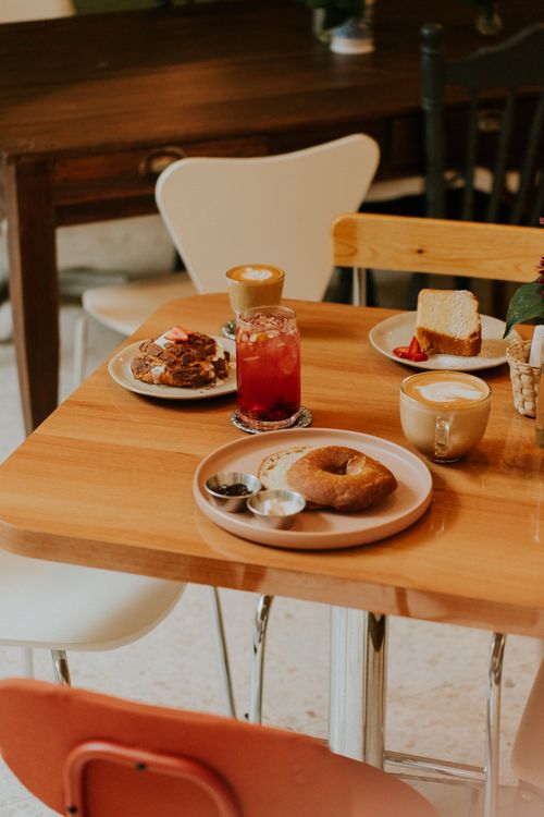 Free Warm café setting with bagels, coffee, and dessert on a wooden table, evoking a cozy breakfast atmosphere. Stock Photo
