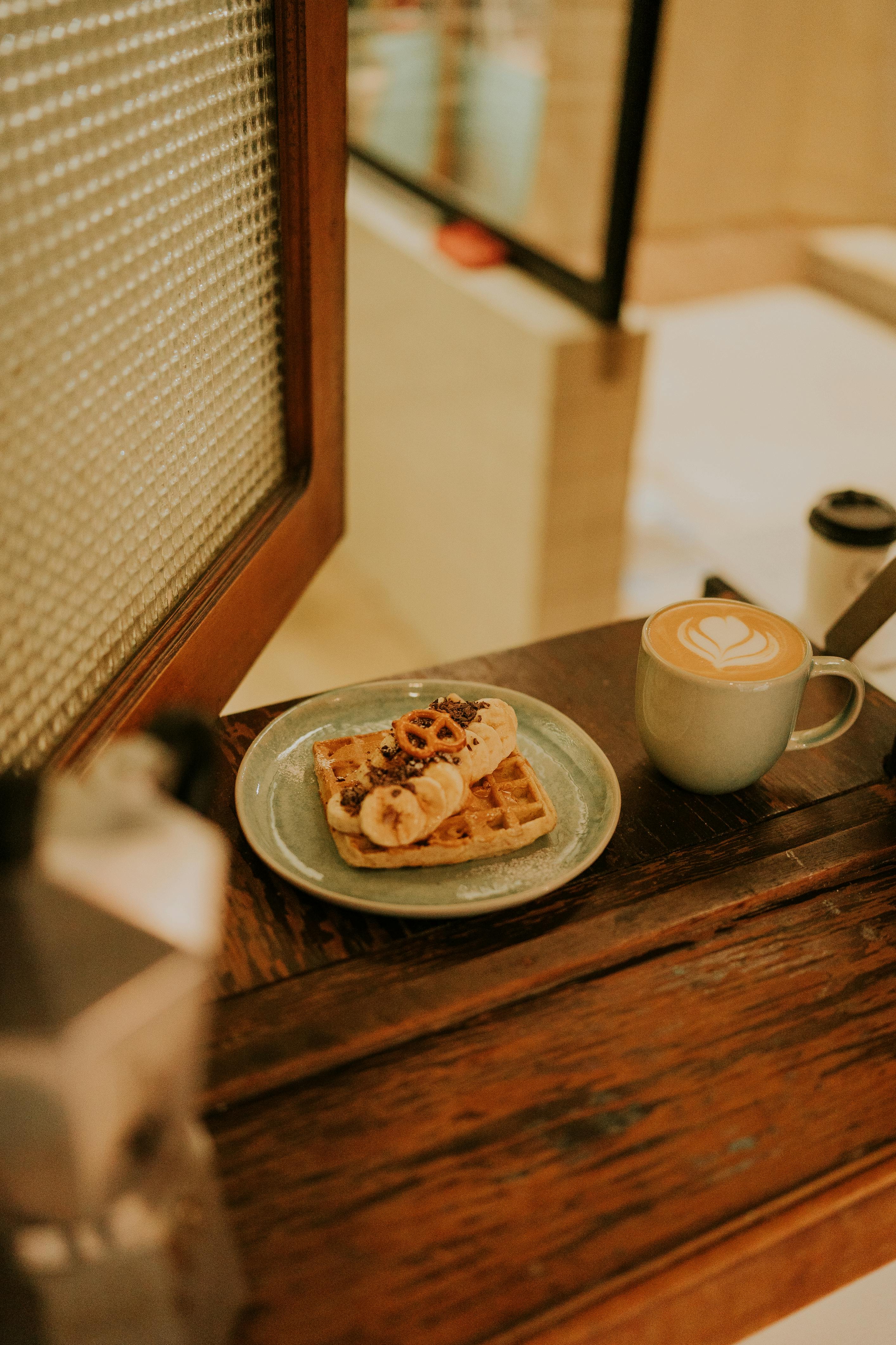 a waffle and coffee on a table next to a window