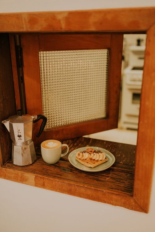 Free Enjoy a cozy café vibe with a latte, waffle, and espresso pot in a rustic wooden setting. Stock Photo
