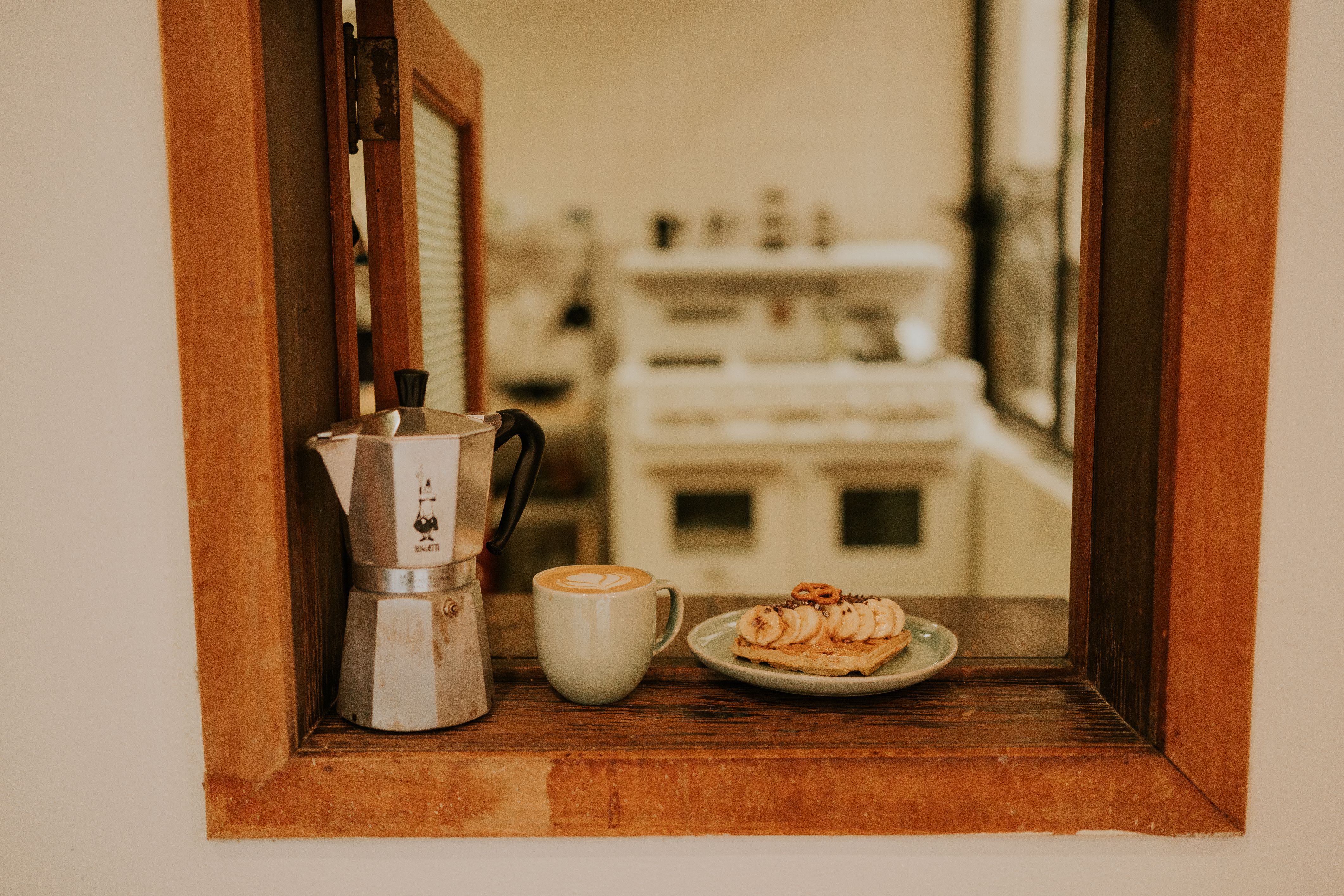 Warm kitchen scene with coffee, espresso maker, and pastries on a wooden windowsill.