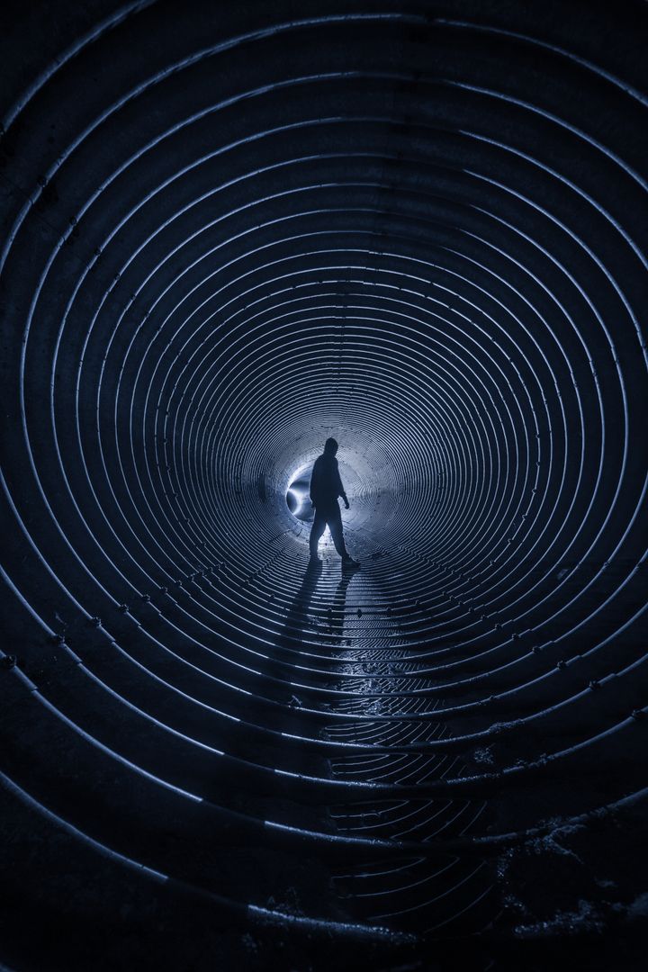 Person walking through a dark tunnel with a flashlight
