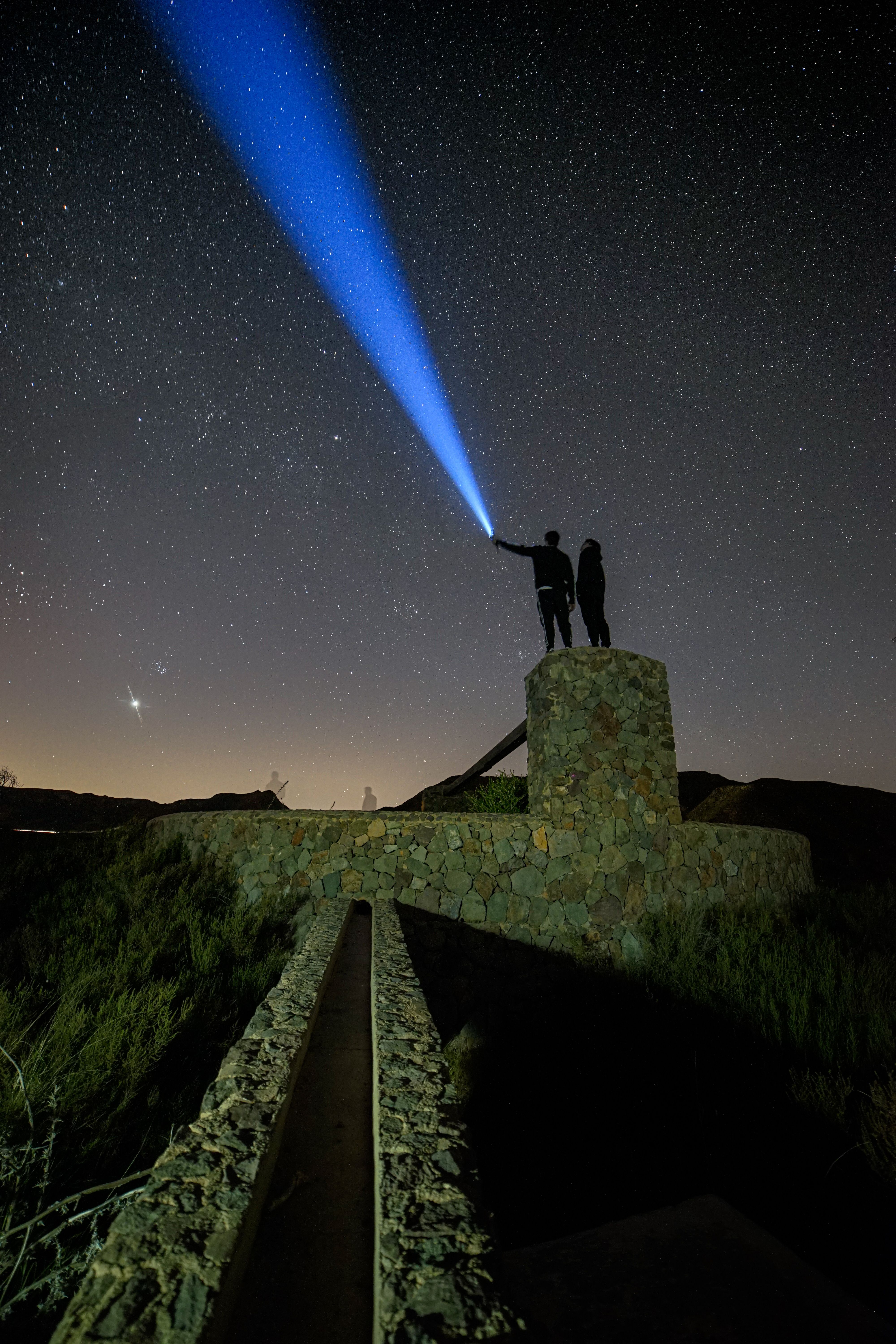 A man and woman standing on top of a hill with a blue light shining ...