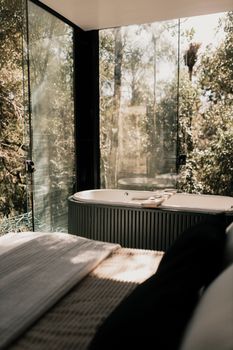Elegant bathroom scene with a bathtub and stunning forest view through glass panels.