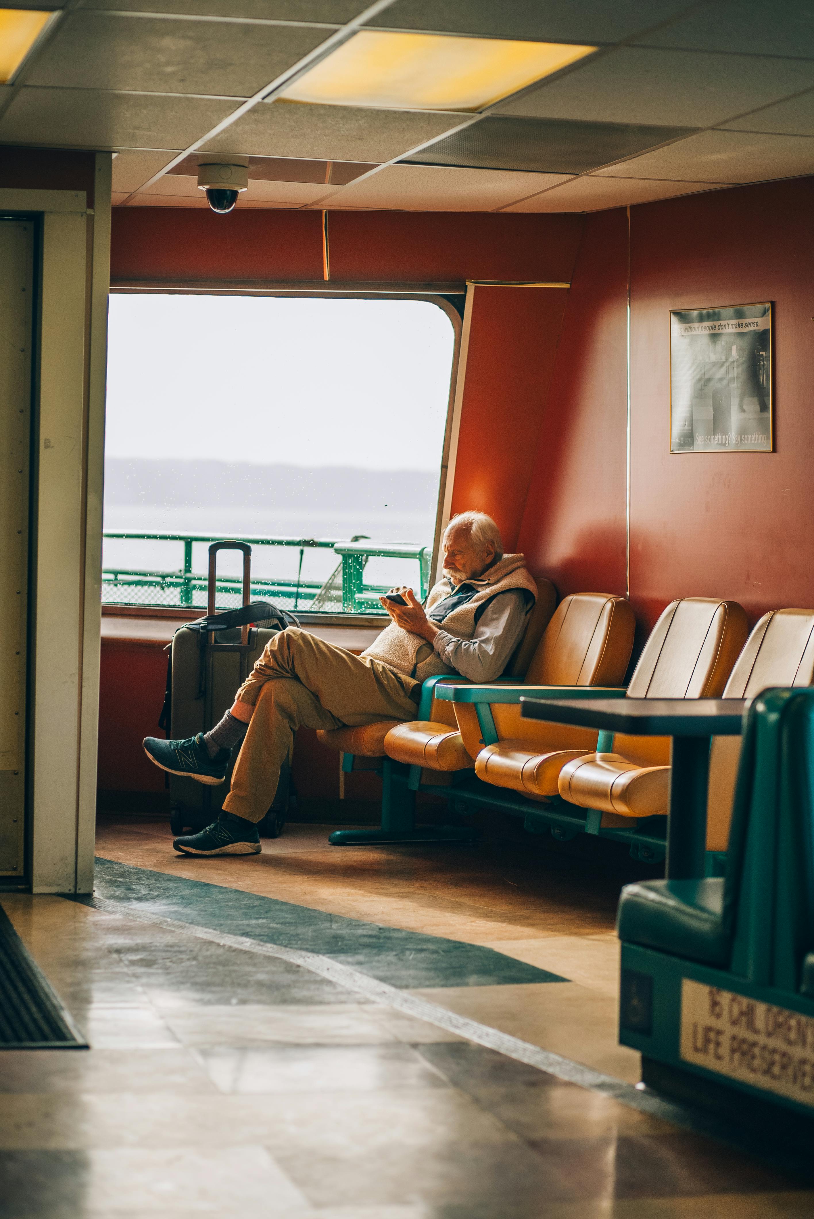 A senior man relaxes on a ferry to Seattle, enjoying his trip with luggage nearby.