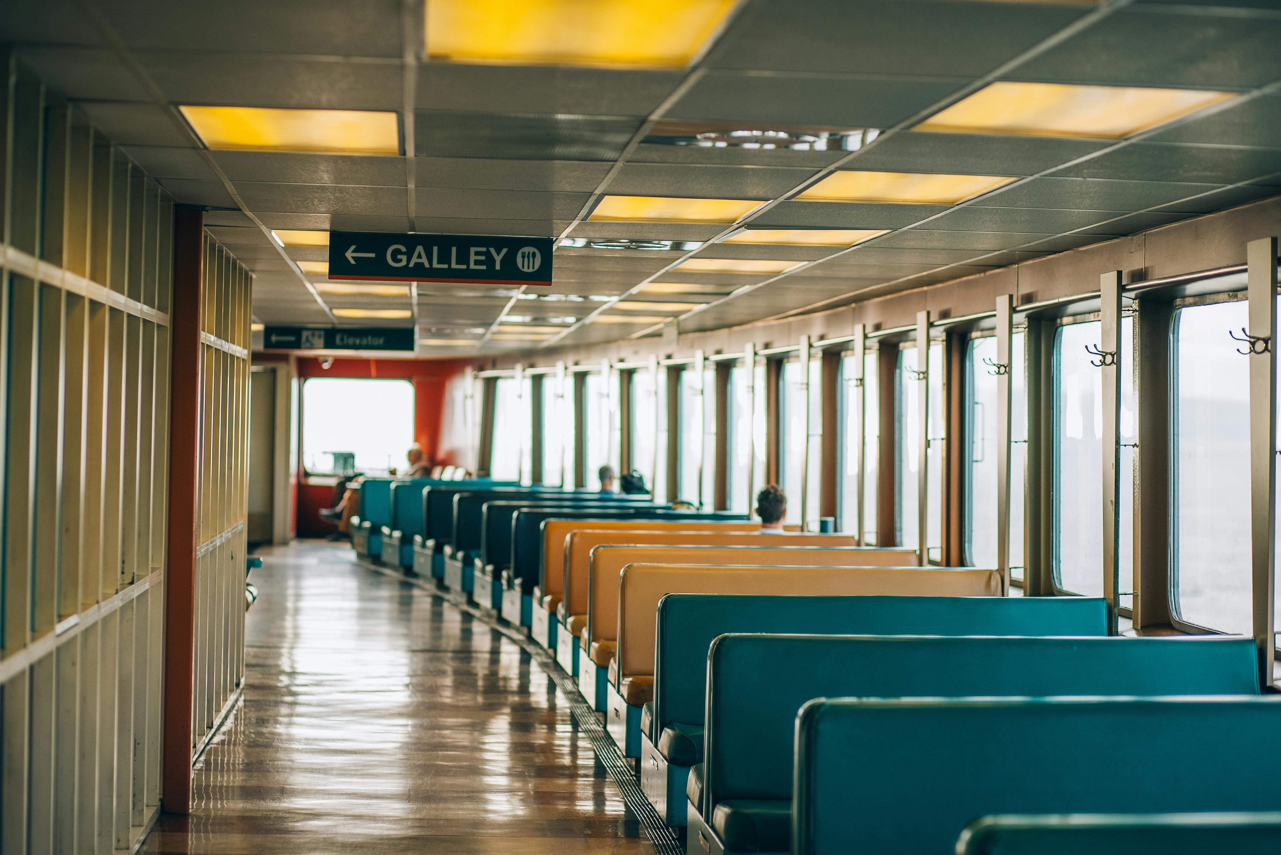 Wide interior view of an empty ferry cabin in Seattle, showcasing colorful seats and signage with a passenger in view.