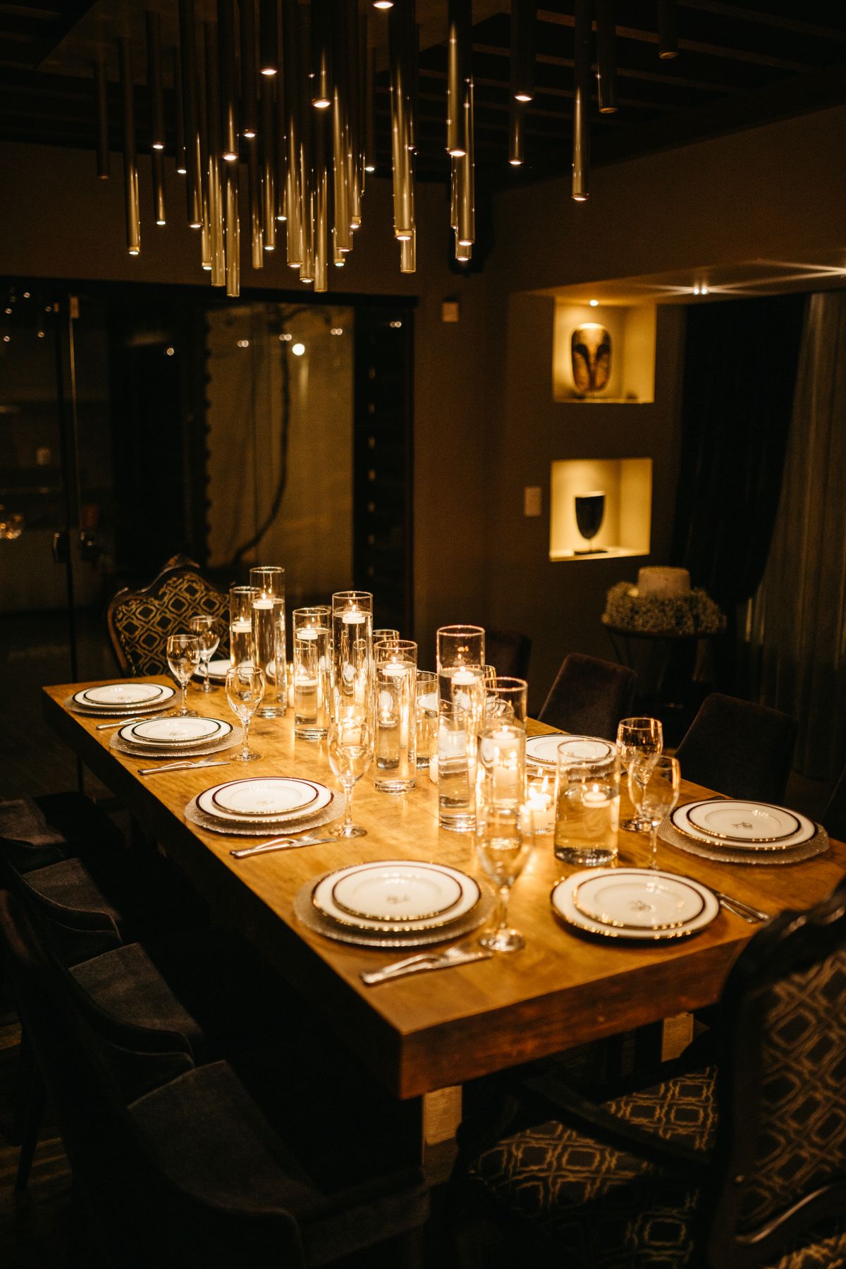 A long private dining table set with glassware under hanging lights