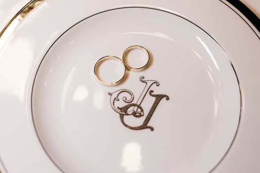 Elegant pair of wedding rings resting on a monogrammed porcelain plate, symbolizing unity and love.