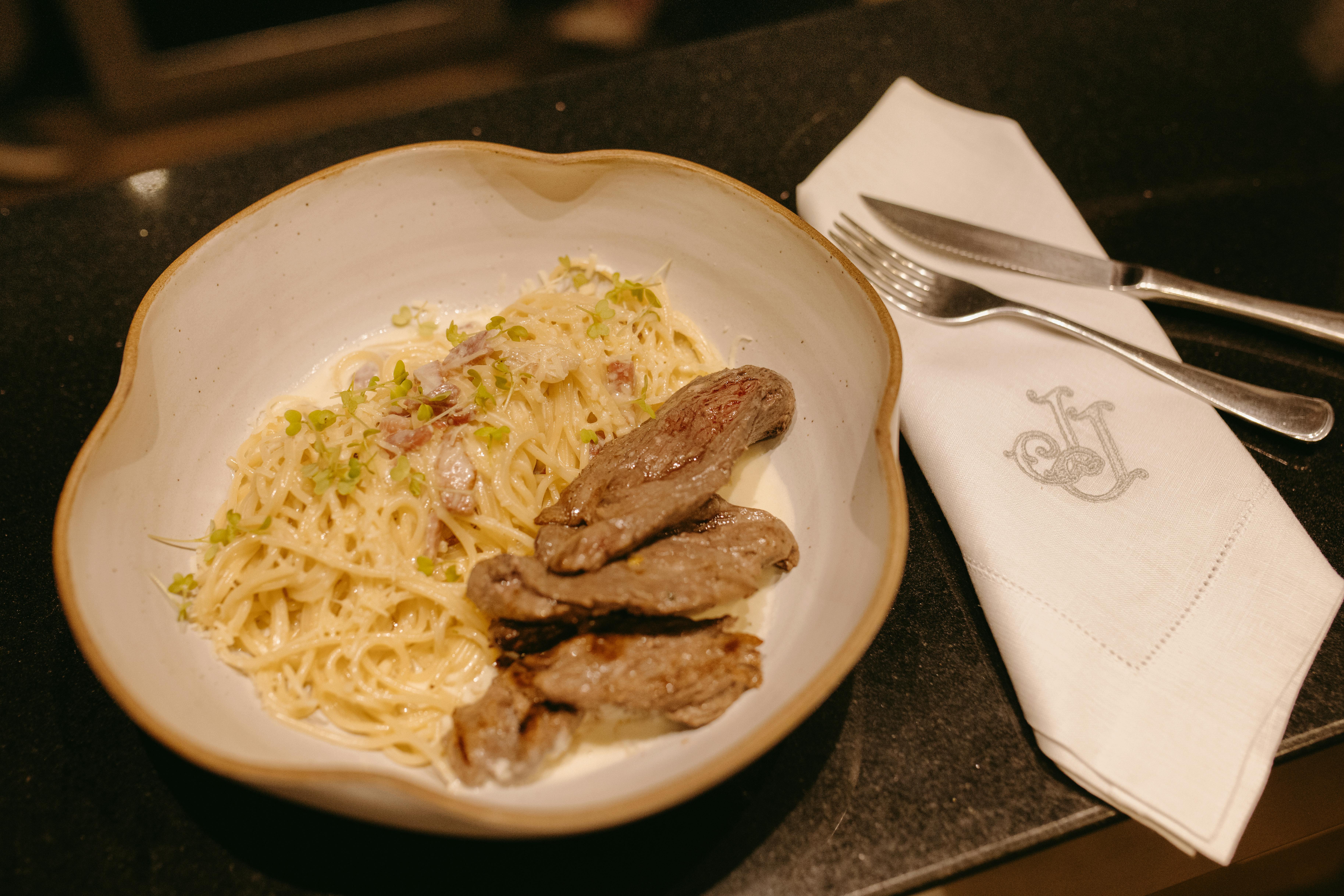 Delicious creamy pasta served with grilled meat on a dining table setting.
