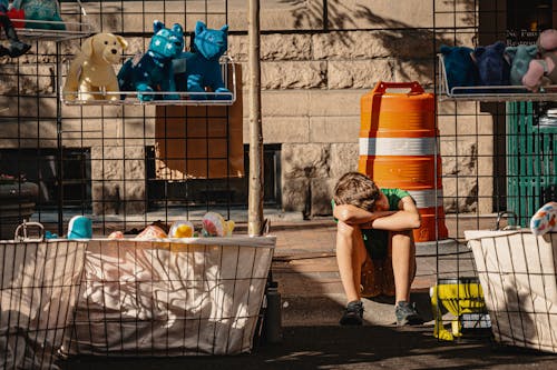 Boy Sits on Pavement Near Toys