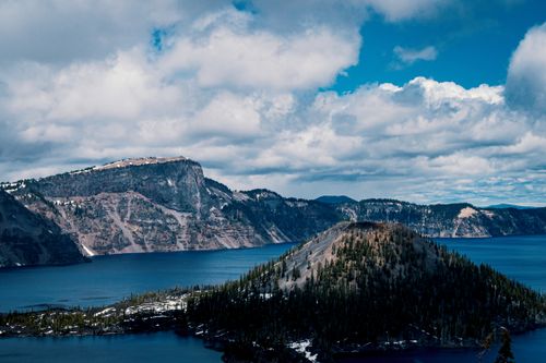 Free Captivating aerial view of Crater Lake with surrounding snow-covered mountains under a blue sky. Stock Photo