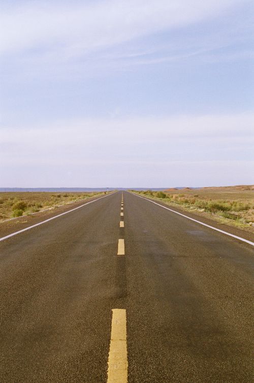 Free A long straight highway stretches into the horizon under a clear blue sky. Stock Photo
