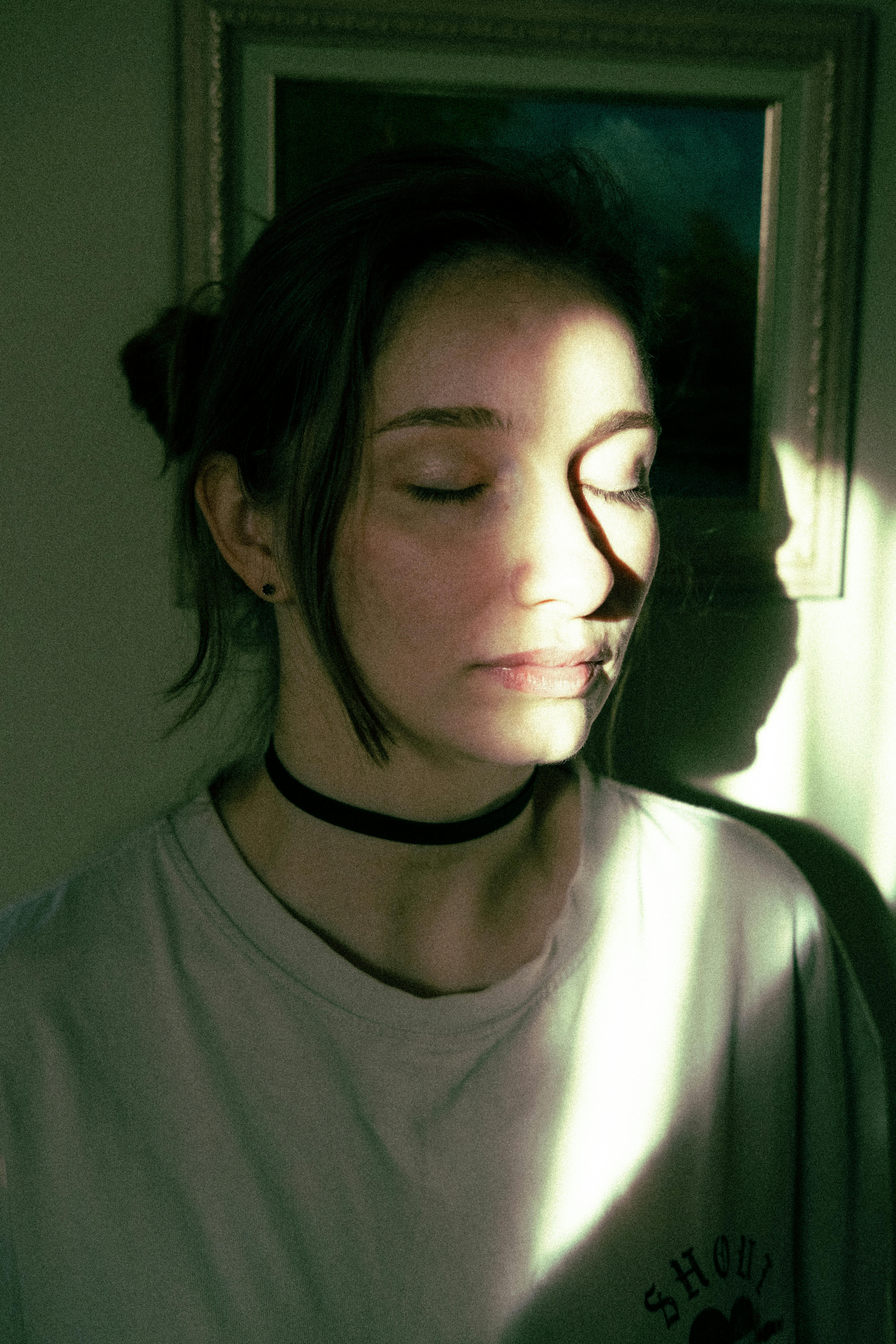 An artistic portrait of a young woman with closed eyes, bathed in soft light indoors.