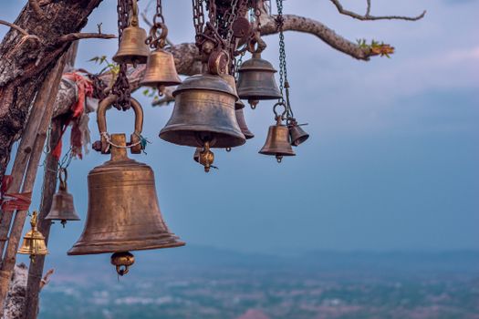 Photograph of bronze bells hanging from a tree branch with a scenic backdrop, symbolizing spirituality.