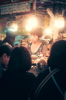 A bustling street food stall at a night market in Seoul with people enjoying Korean cuisine.