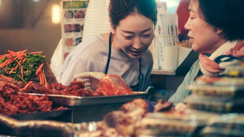 A vibrant scene capturing Korean tradition with women in a bustling Seoul market stall.