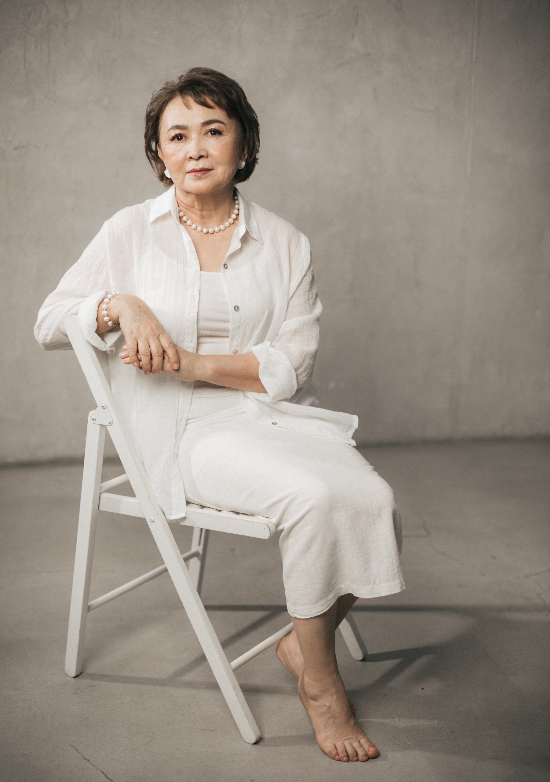 Sophisticated portrait of a mature woman sitting on a chair in a minimalist setting.