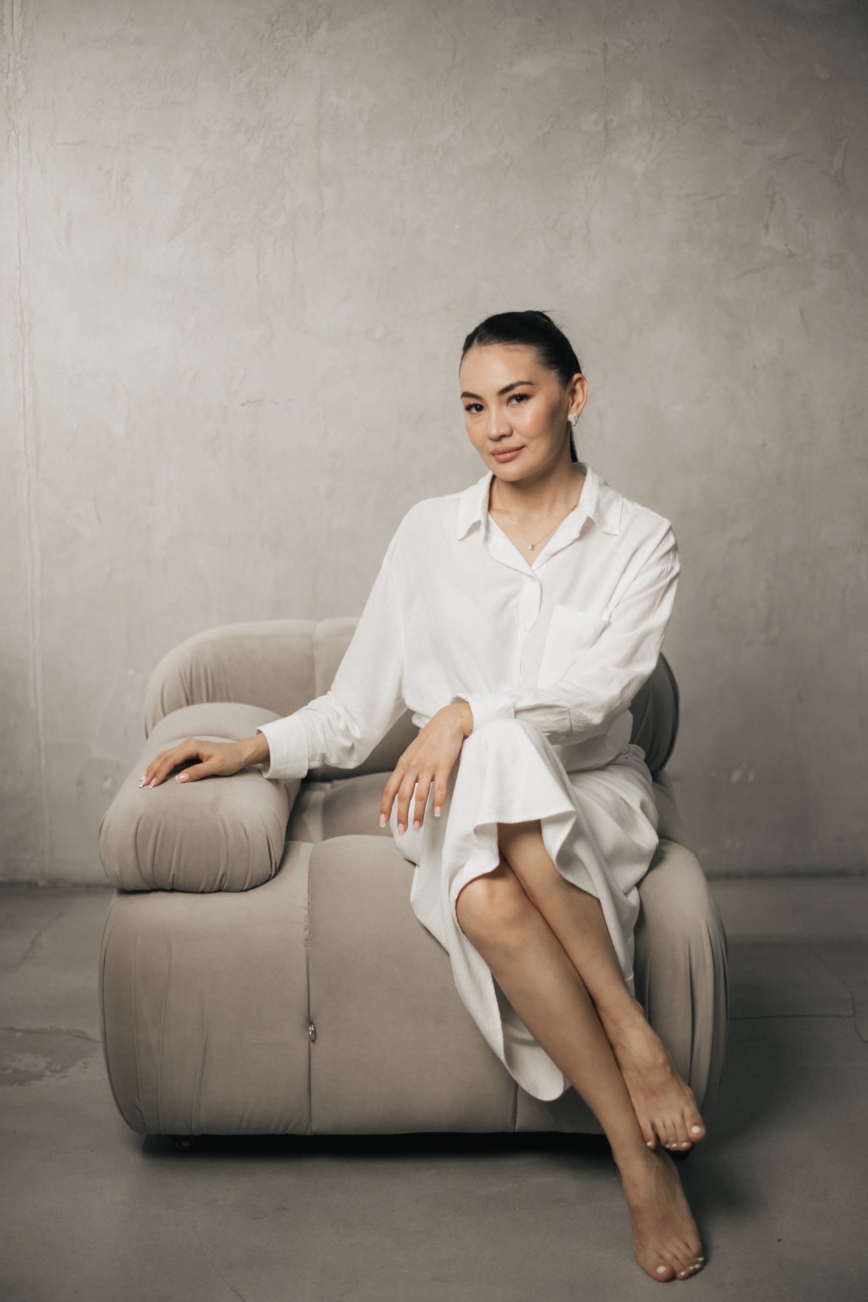 A stylish woman in white attire sitting on a modern chair, embodying elegance and sophistication.