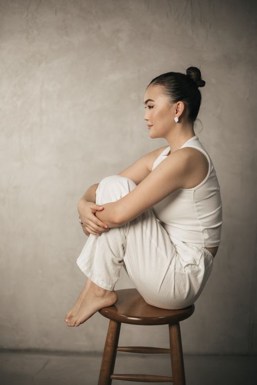 Free Sophisticated woman in white attire sitting gracefully on a stool against a minimalist background. Stock Photo