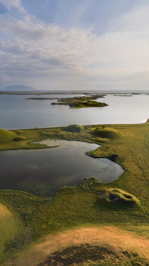Free A tranquil aerial view of lush green islands surrounded by a calm lake under a cloudy sky. Stock Photo