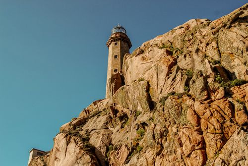Free Lighthouse perched on rugged cliffs with a clear blue sky, perfect for travel and adventure themes. Stock Photo