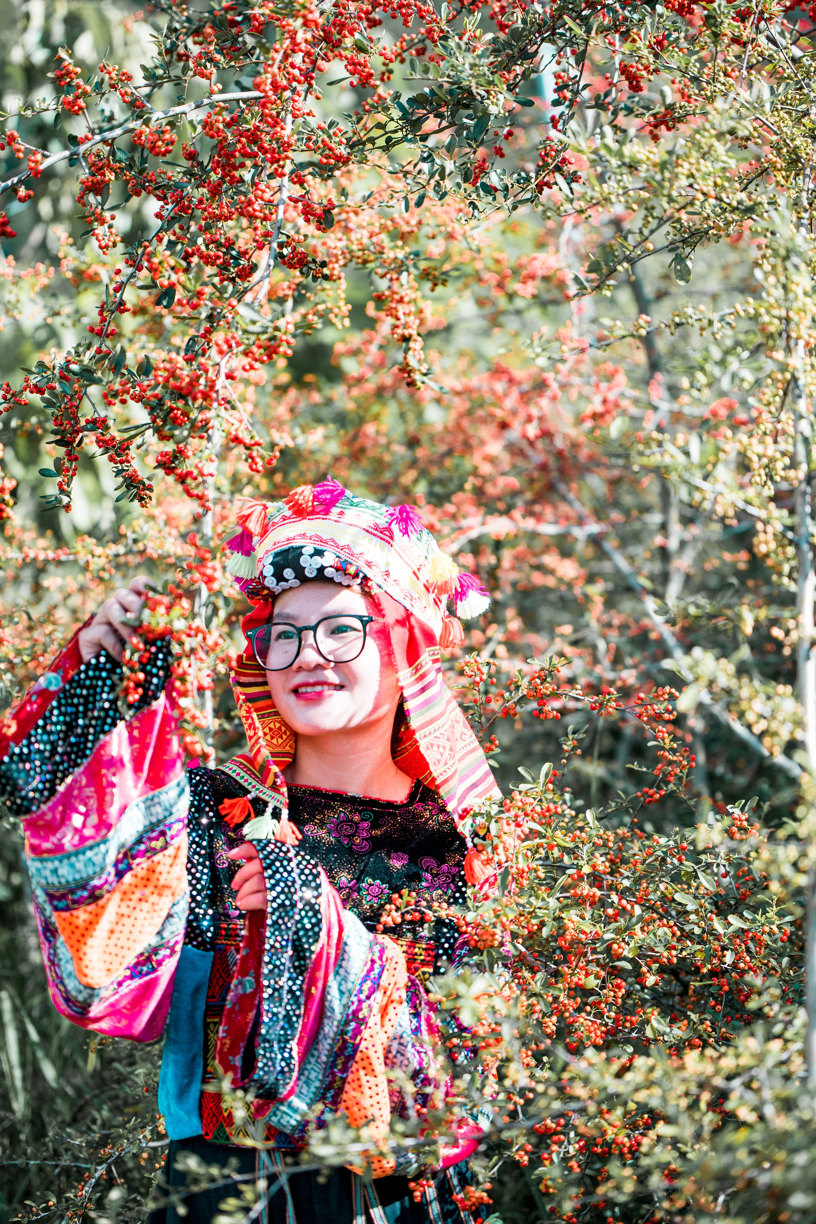 Woman in colorful traditional clothing enjoying nature surrounded by autumn leaves.