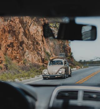 A vintage car driving on an open road through rocky terrain, showcasing a classic travel experience.