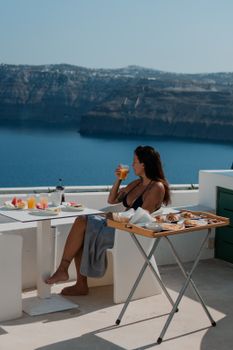 Woman enjoying a breakfast on a terrace with stunning ocean views in Santorini, Greece.