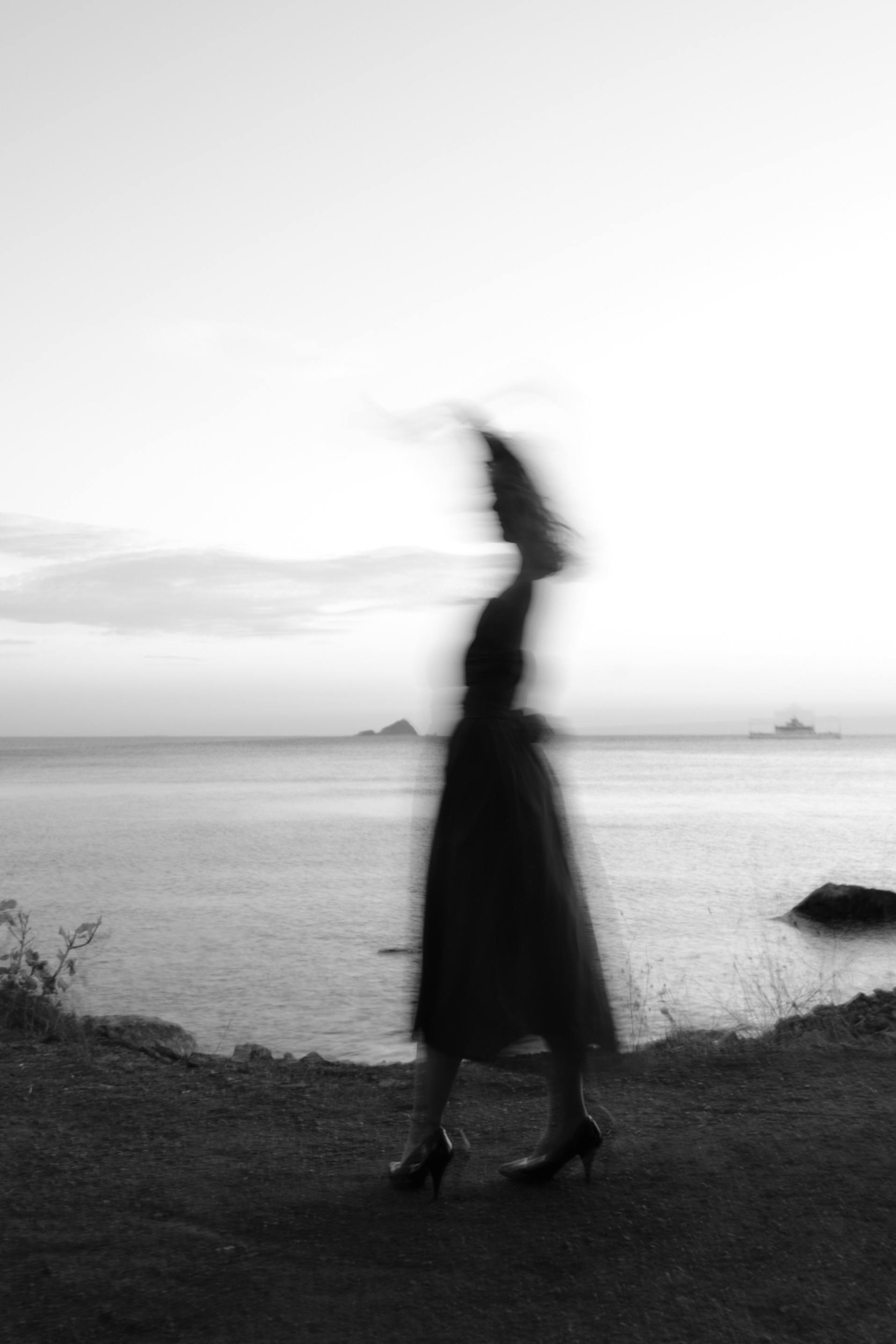 Artistic black and white silhouette of a woman by the sea with a blurred effect at dusk.