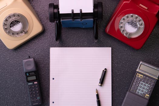 Vintage office equipment with rotary phones, notebook, and calculator flat lay composition.