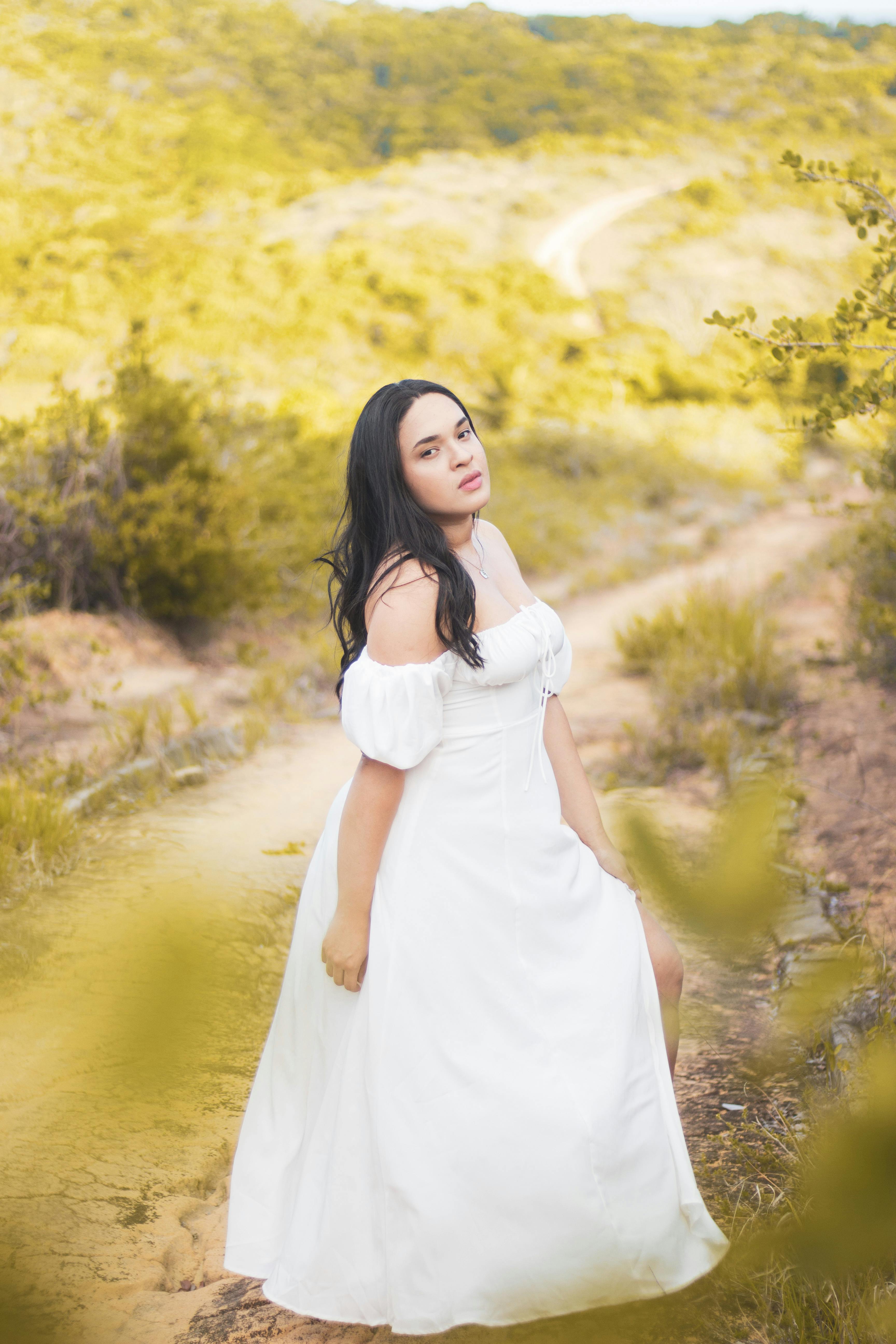 a woman in a white dress is walking down a dirt road