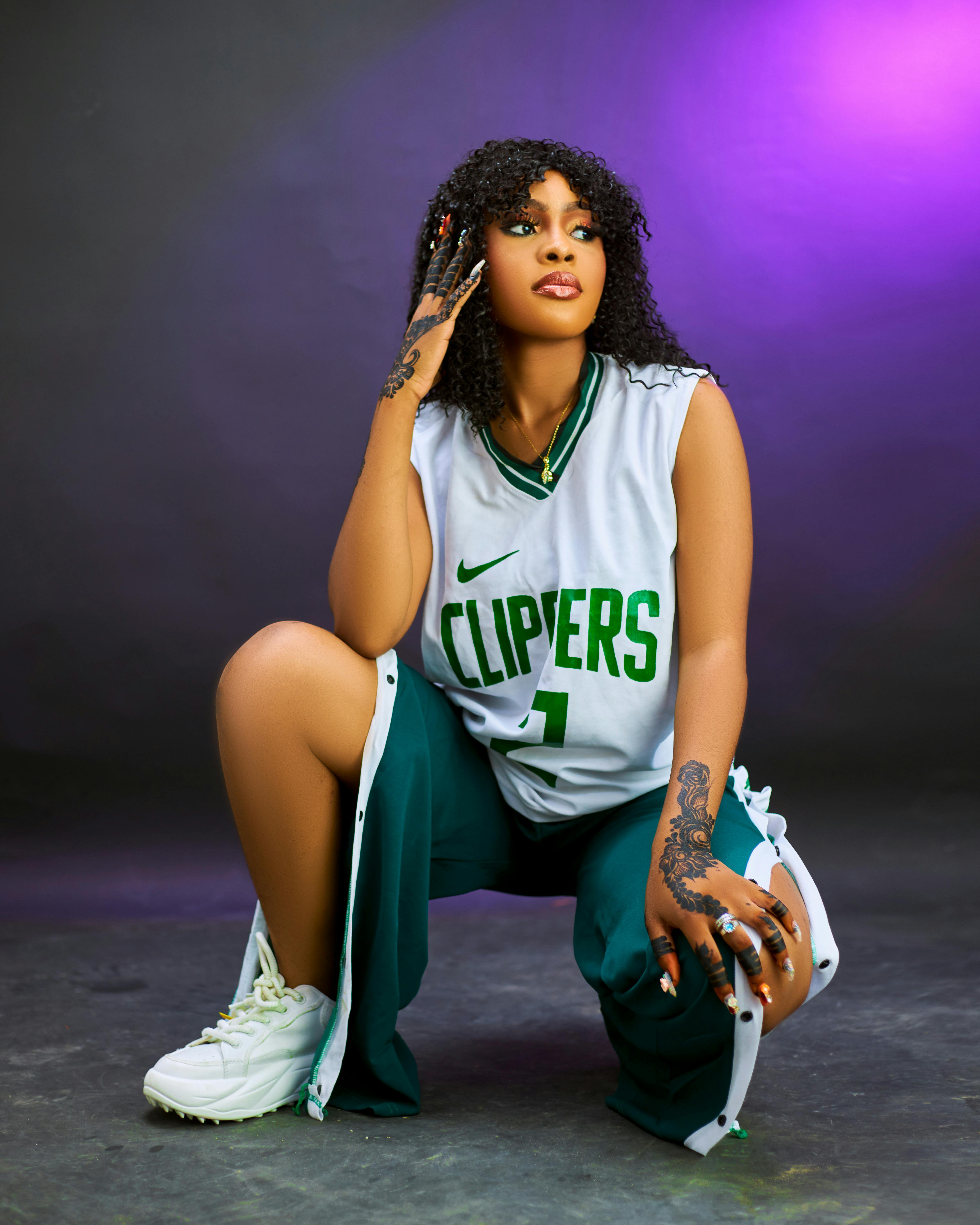 Stylish woman wearing a Clippers jersey and sneakers posing against a vibrant background.