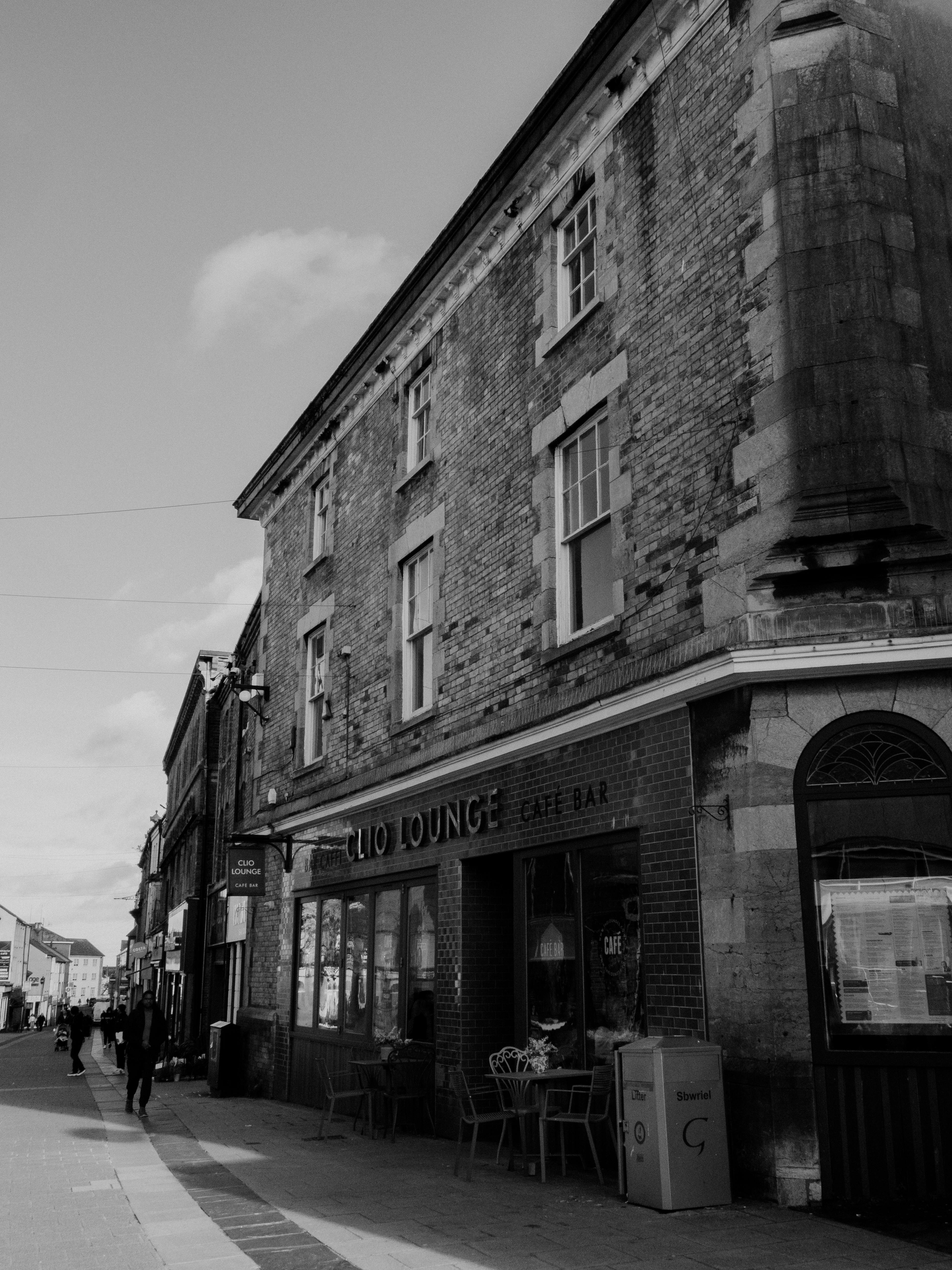 A black and white photo of a historic city street featuring old brick buildings and subtle urban activity.