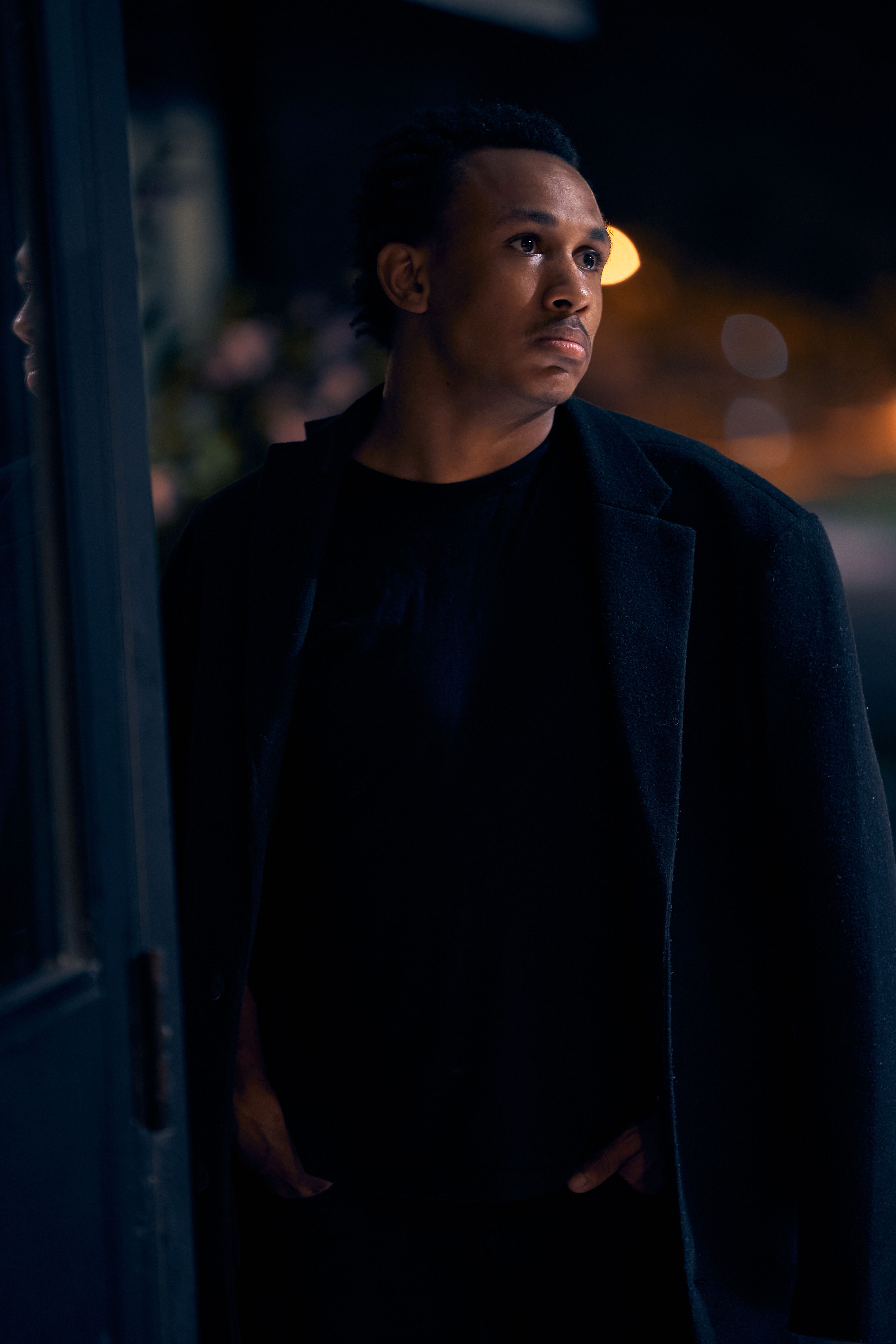 A thoughtful man gazes with intensity in a nighttime city scene, embodying modern fashion and emotion.