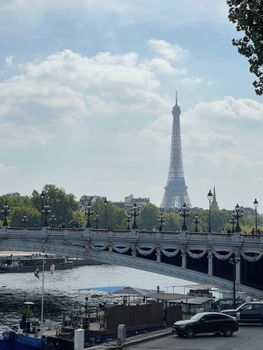 Scenic view of the Eiffel Tower from a Parisian bridge over the river on a sunny day.