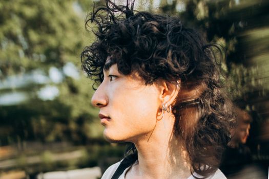 Side profile portrait of a young adult with curly hair and earrings outdoors in natural light.