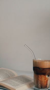 Glass of iced coffee and an open book on a cozy table setting.