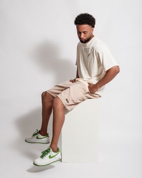 Fashionable young man sitting in studio wearing casual summer outfit.