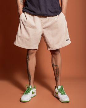 Stylish man in shorts and sneakers posing in a studio with an orange background.