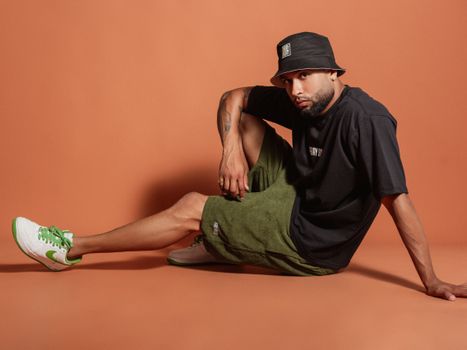 Stylish young man in a studio, wearing casual streetwear and a hat.