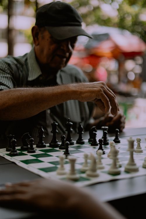 Free An elderly man concentrates while playing chess outdoors, emphasizing strategy and leisure. Stock Photo