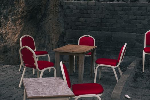 Empty outdoor seating area with red chairs and a wooden table against a brick wall.